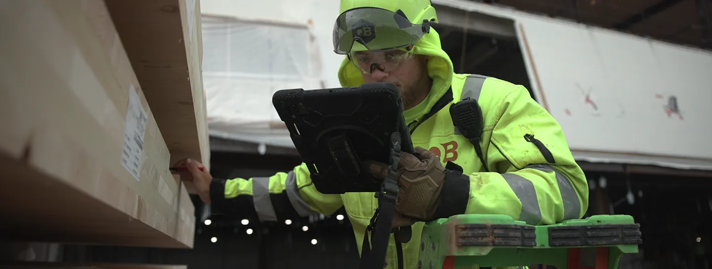 A construction worker in a high-visibility jacket uses a tablet at a building site.