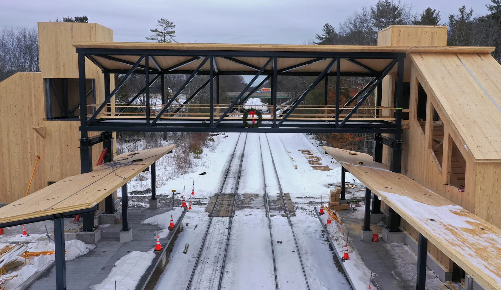 A construction worker stands on a partially built covered bridge over snowy train tracks.