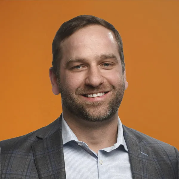 Man smiling, wearing a business suit, against an orange background.