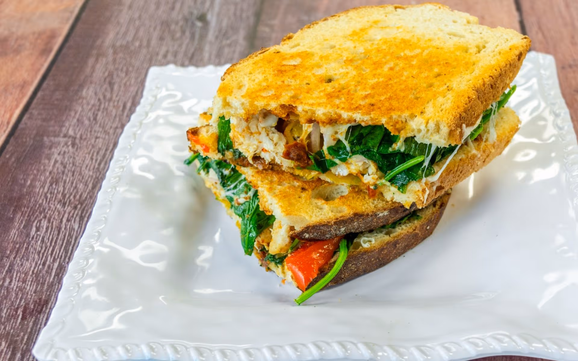 Grilled sandwich with spinach, roasted red peppers, and grilled chicken on white plate.