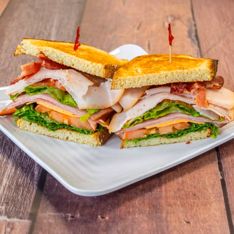 Club sandwich with turkey, ham, lettuce, tomato, bacon on toasted bread halves with red toothpicks.