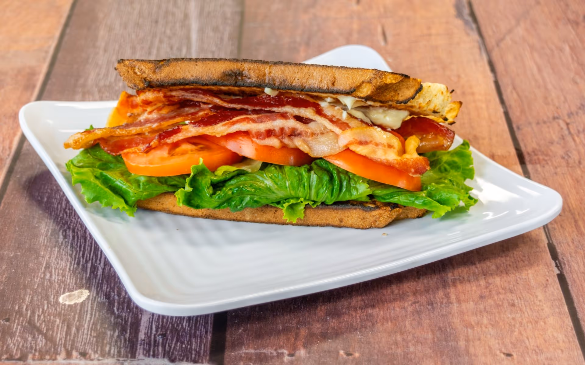 Bacon, lettuce, and tomato sandwich on toasted bread served on a white plate.