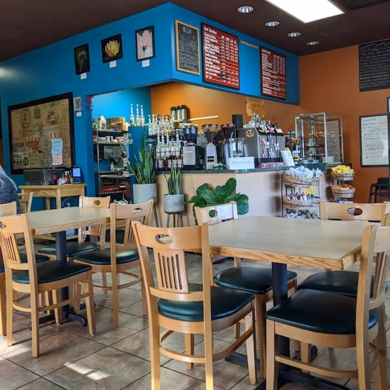 Cozy cafe interior with wooden tables, chairs, plants, and a coffee counter with menu boards.