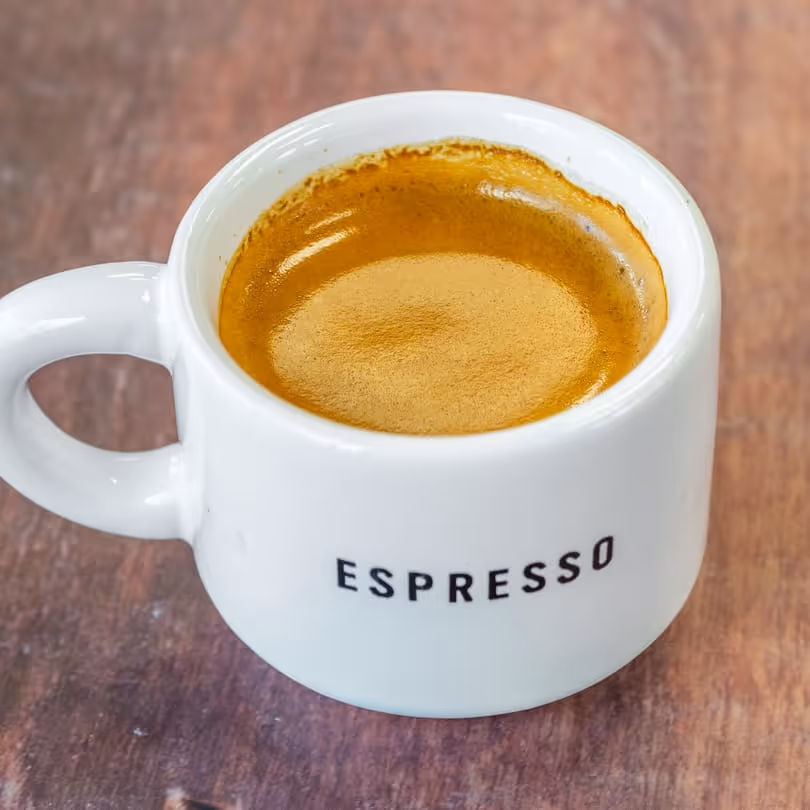 White ceramic cup with the word ESPRESSO filled with fresh espresso on a wooden surface.