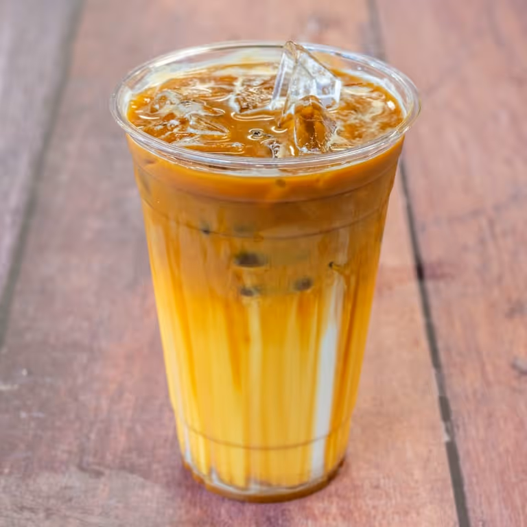 Iced coffee drink with milk in a clear plastic cup on a wooden surface.