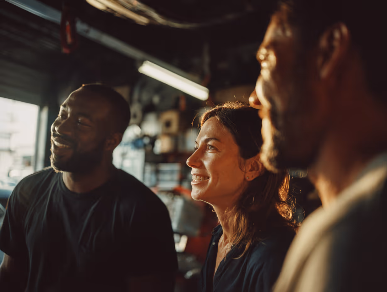 Three people smiling and talking in a warmly lit indoor setting with blurred background.
