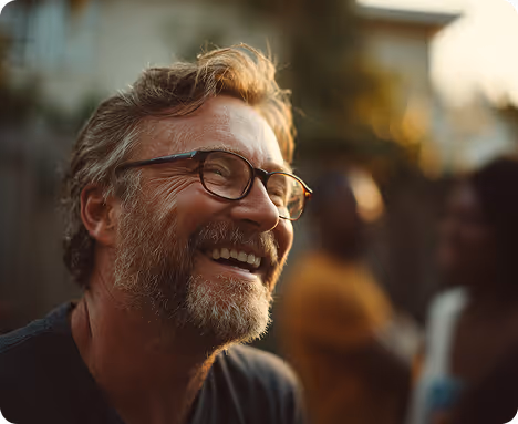Smiling middle-aged man with glasses and beard outdoors with blurred people in background.