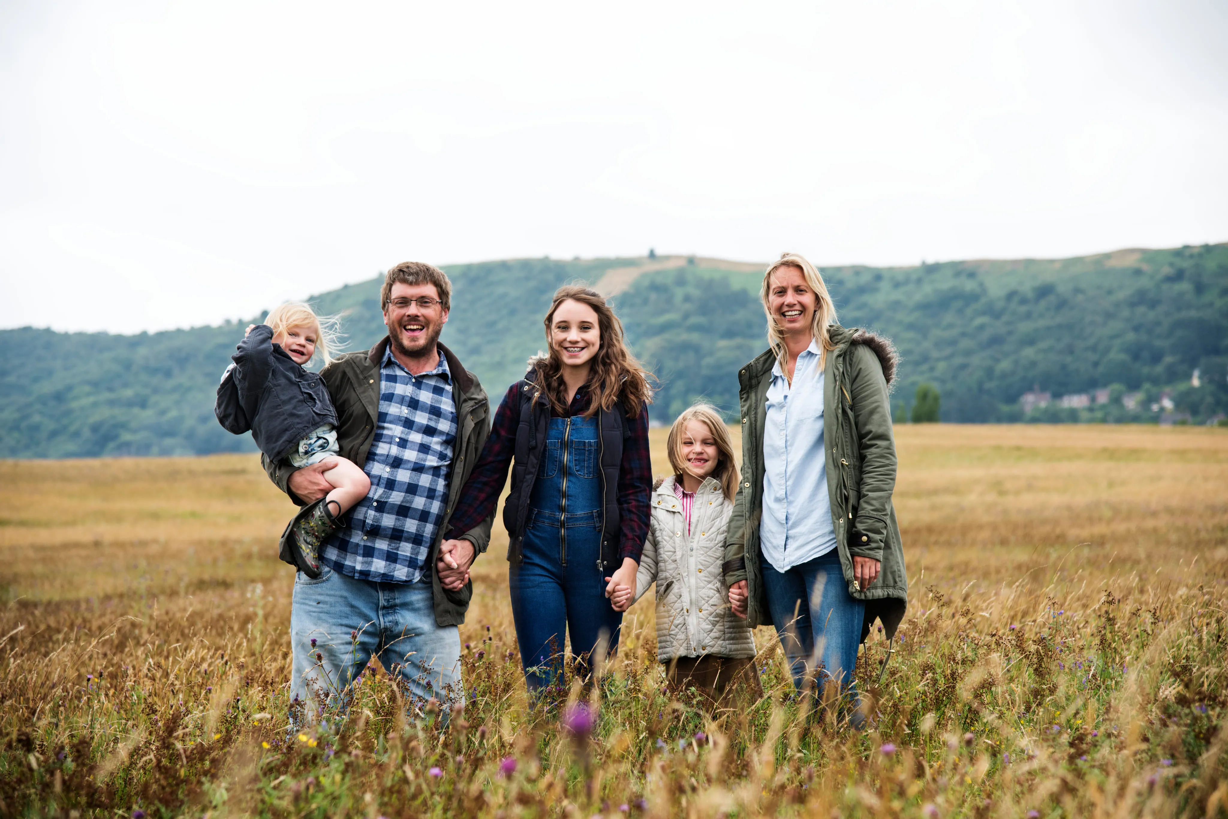 Smiling family of five standing in a grassy field with hills in the background.