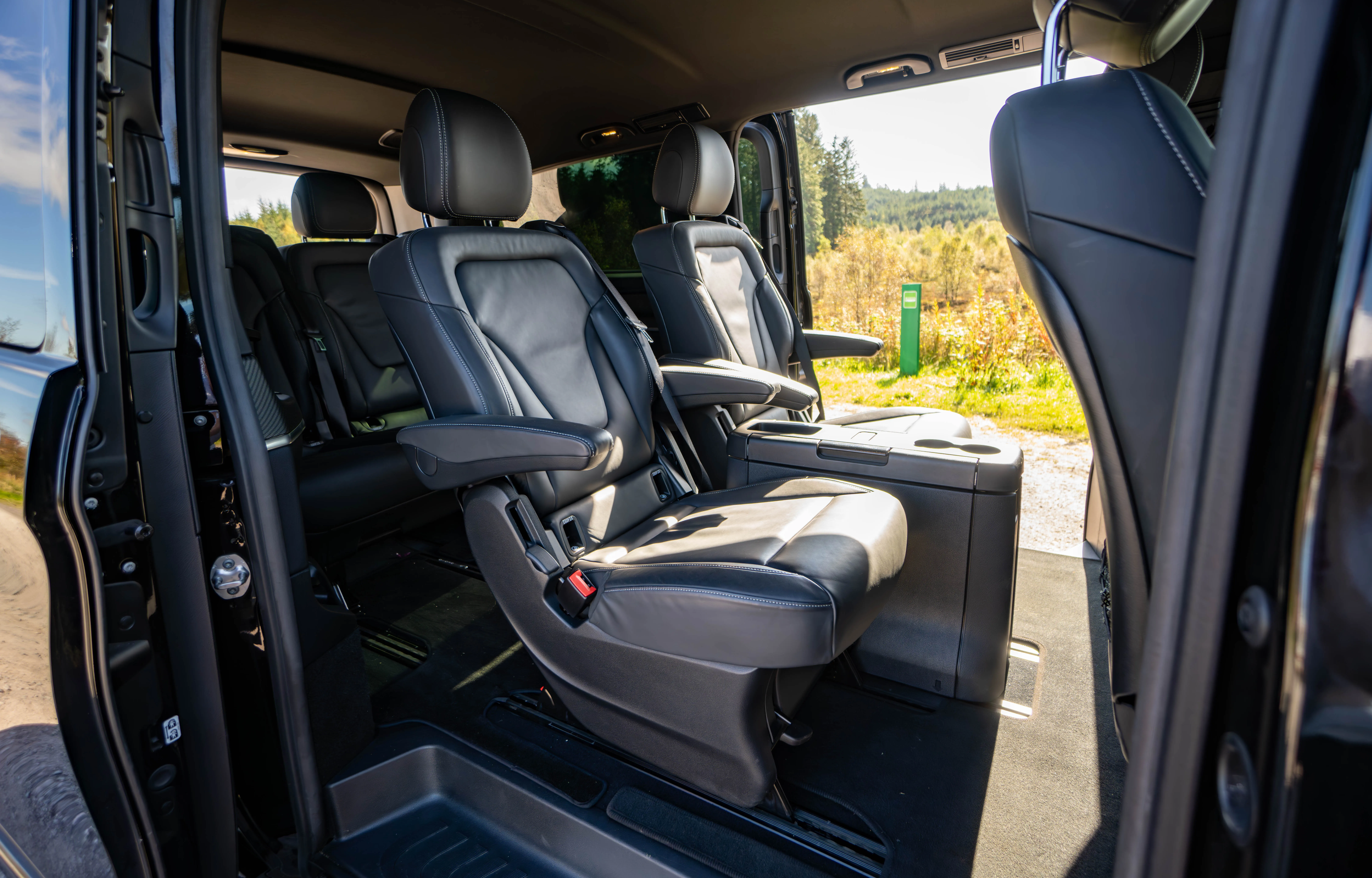 Interior of a vehicle showing black leather captain seats with armrests and a console in between.