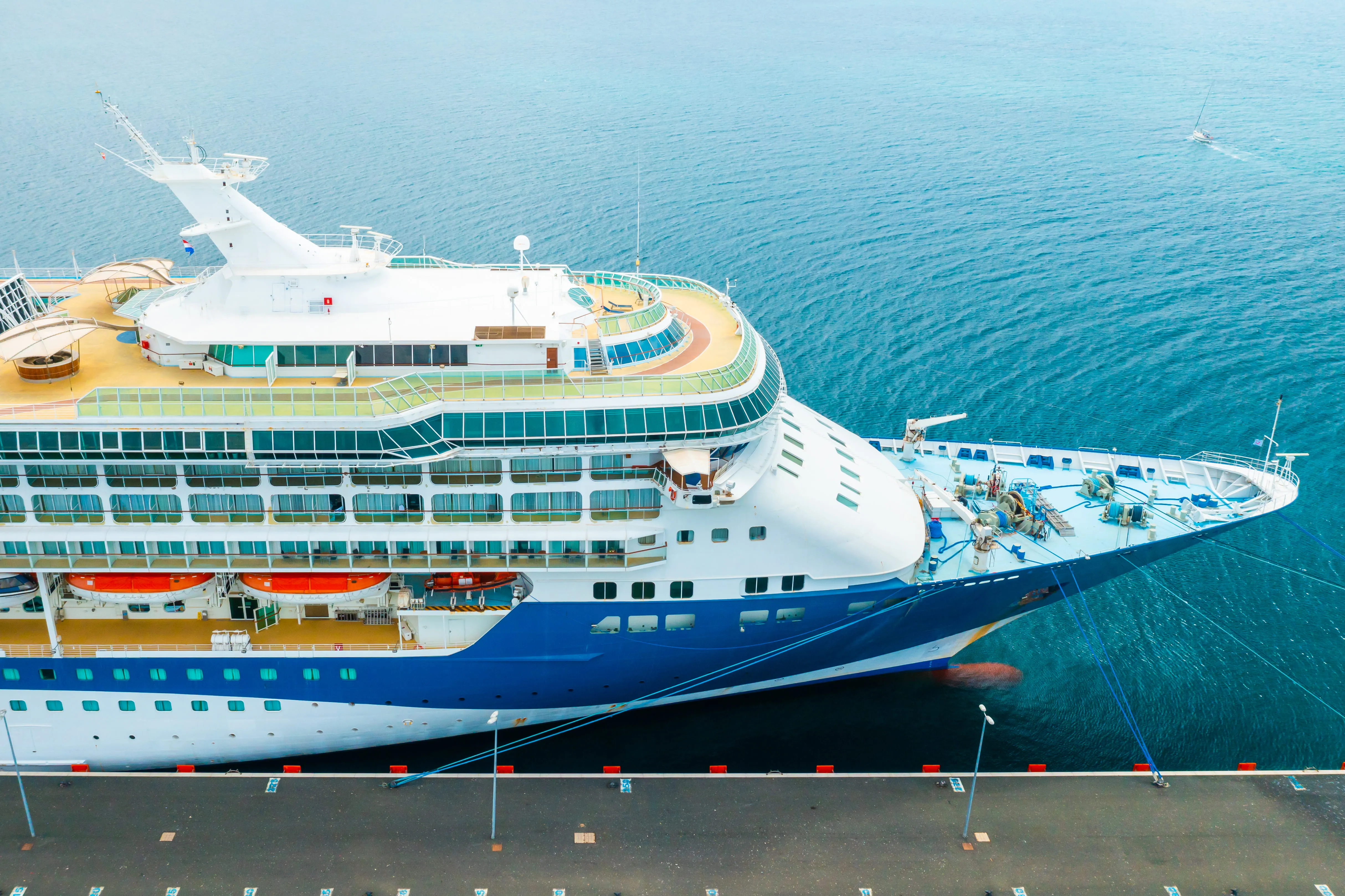 Aerial view of a large luxury cruise ship docked at a pier with calm blue water surrounding it.
