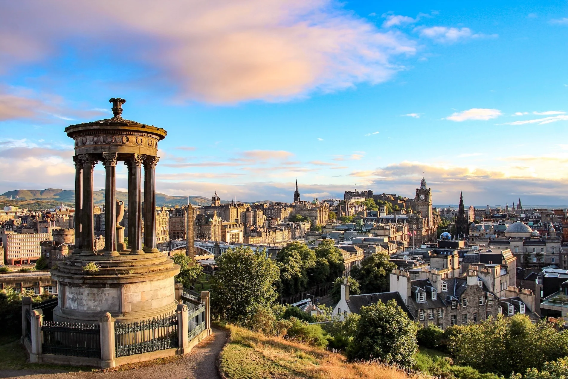 View of Edinburgh cityscape at sunrise with Dugald Stewart Monument in foreground atop Calton Hill.
