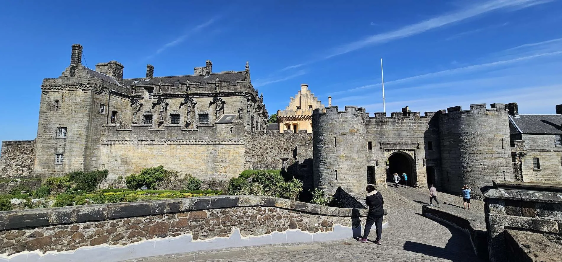 Historic stone castle with arched entrance, round towers, and people walking on a cobblestone path.