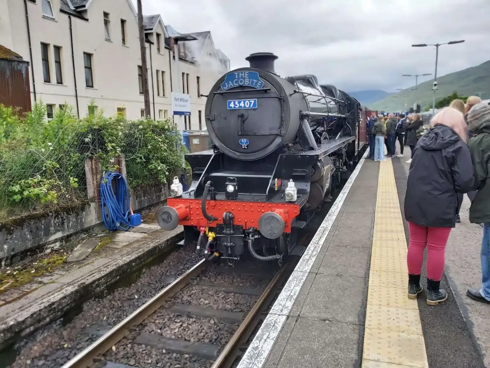 Black steam train labeled The Jacobite at Fort William station with passengers on the platform.