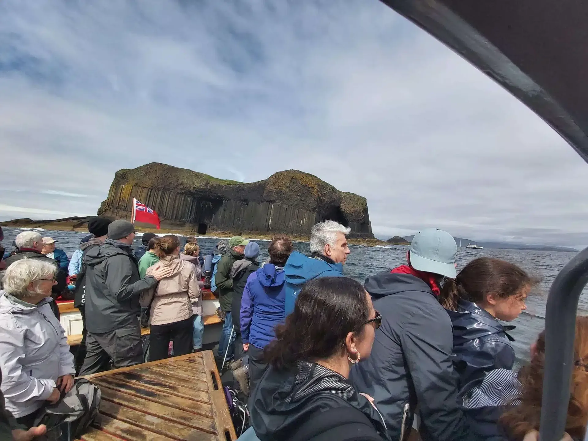 Group of people on a boat approaching a rocky island with basalt columns under a cloudy sky.