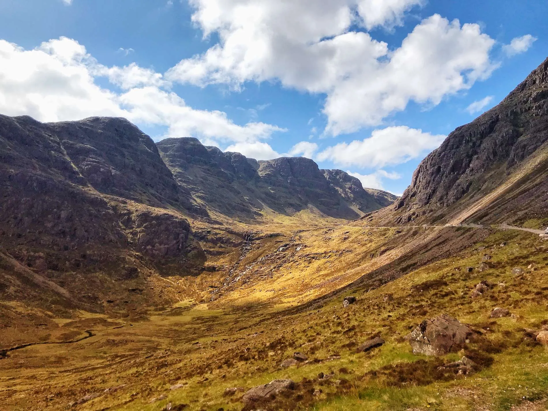 Mountain valley with brown grassy slopes under a blue sky with scattered white clouds.