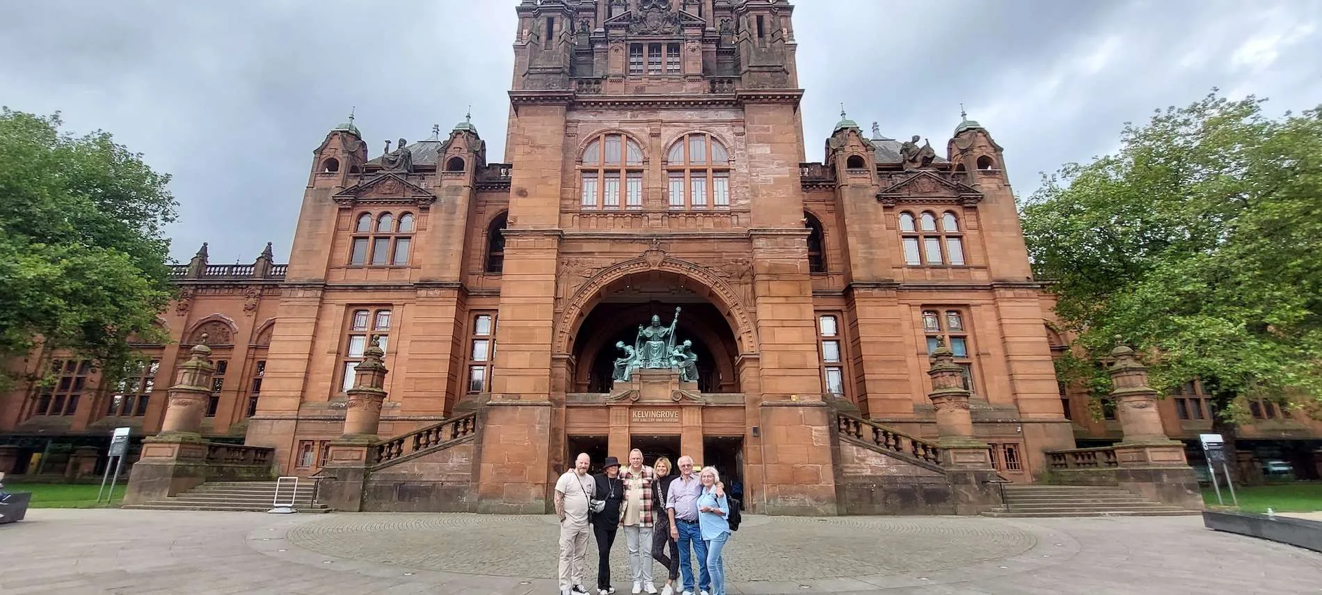 Group of six people standing in front of Kelvingrove Art Gallery and Museum entrance with statues.