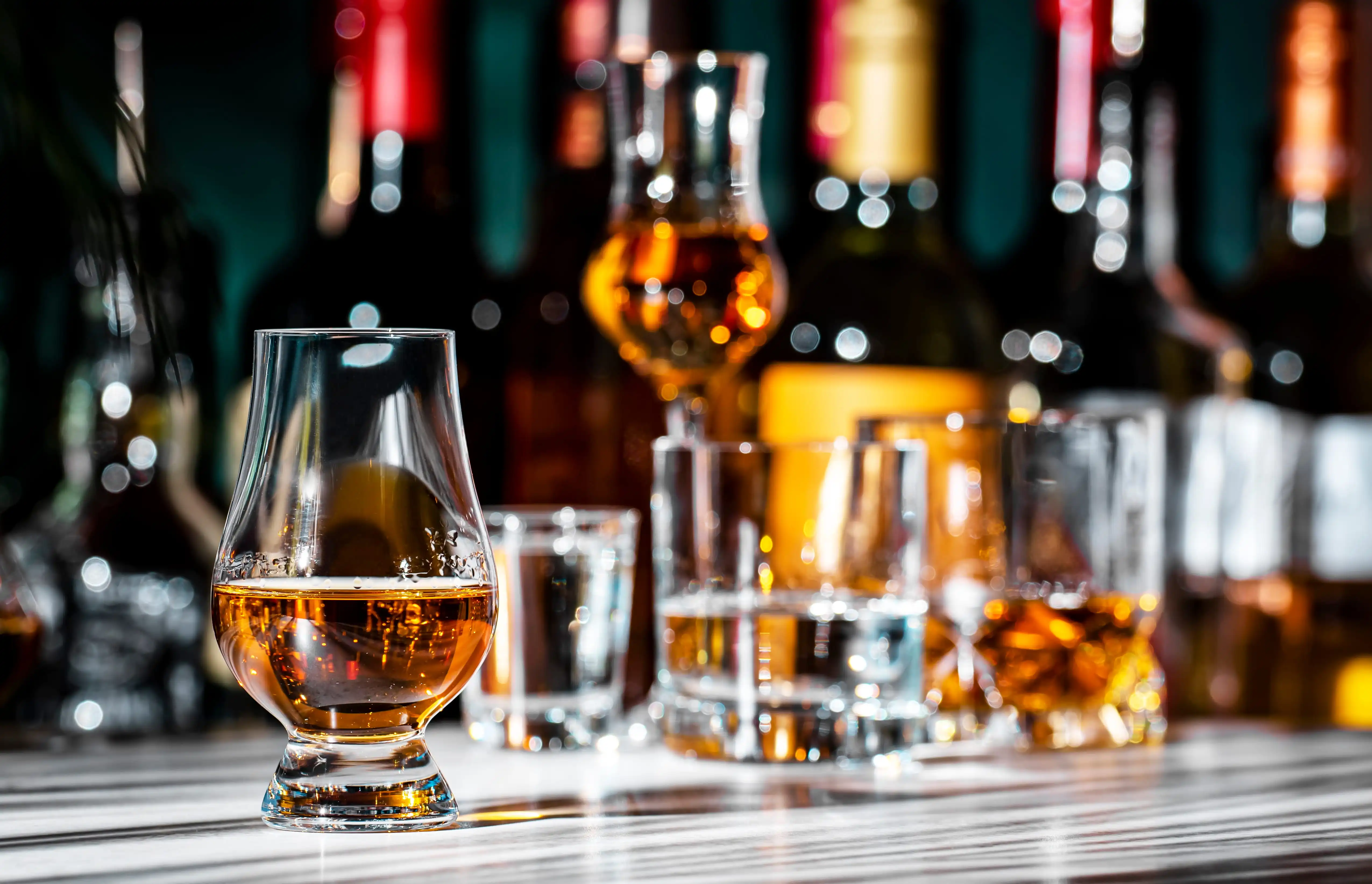 Single malt scotch whisky in a Glencairn glass with blurred bottles and glasses in the background.