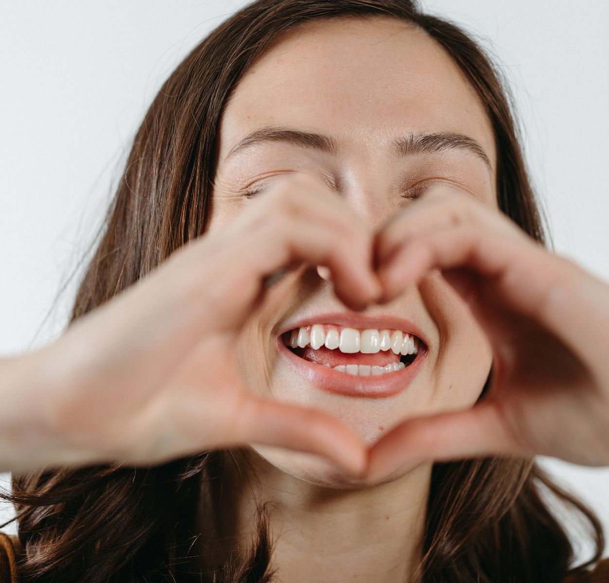 Smiling woman with eyes closed forming a heart shape with her hands in front of her face.
