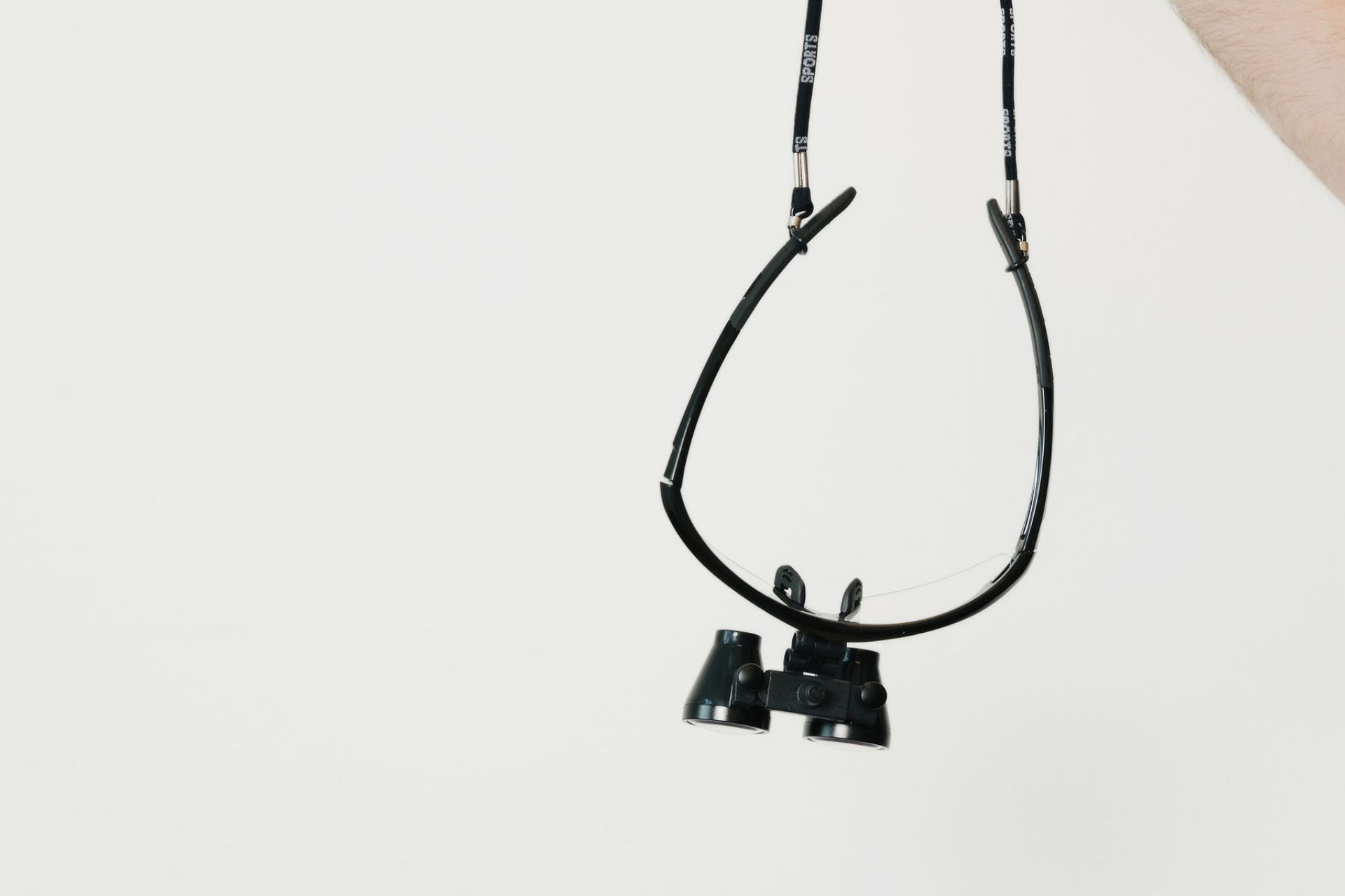 Black magnifying glasses on a strap held by a hand against a plain white background.