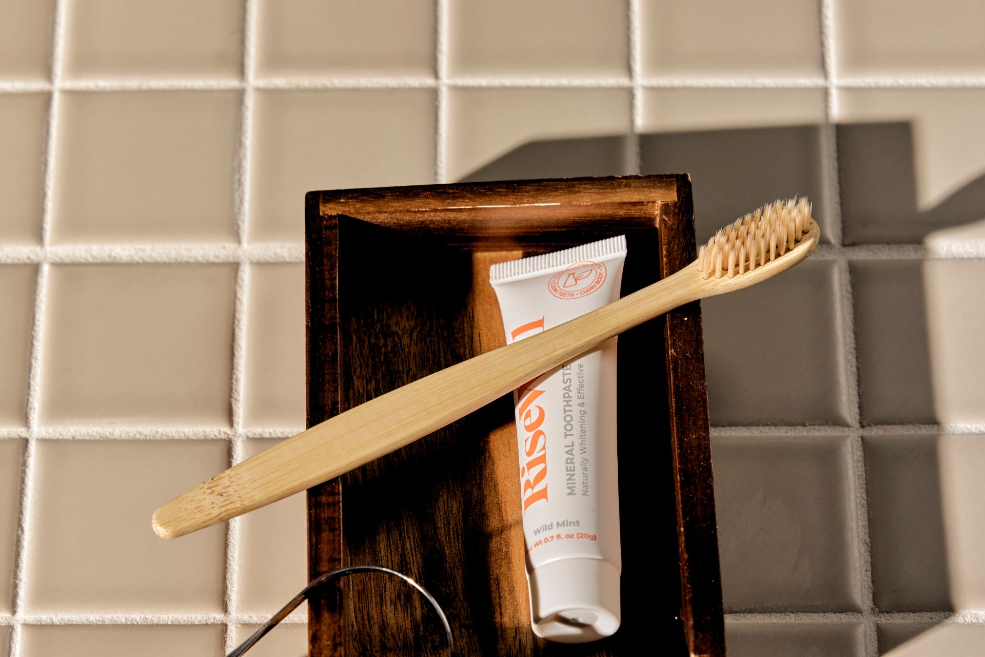 Wooden toothbrush resting on a wooden tray with a tube of Rise mineral toothpaste.