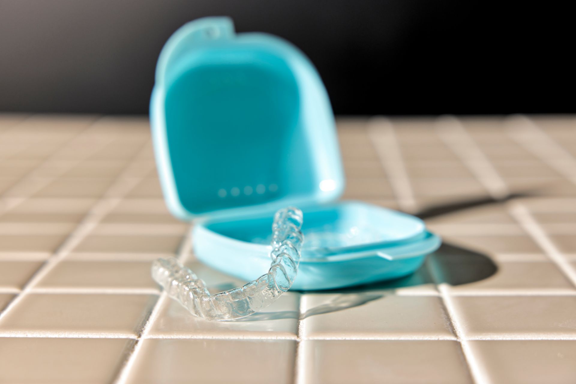 Clear dental aligner resting on white tile next to an open blue storage case.