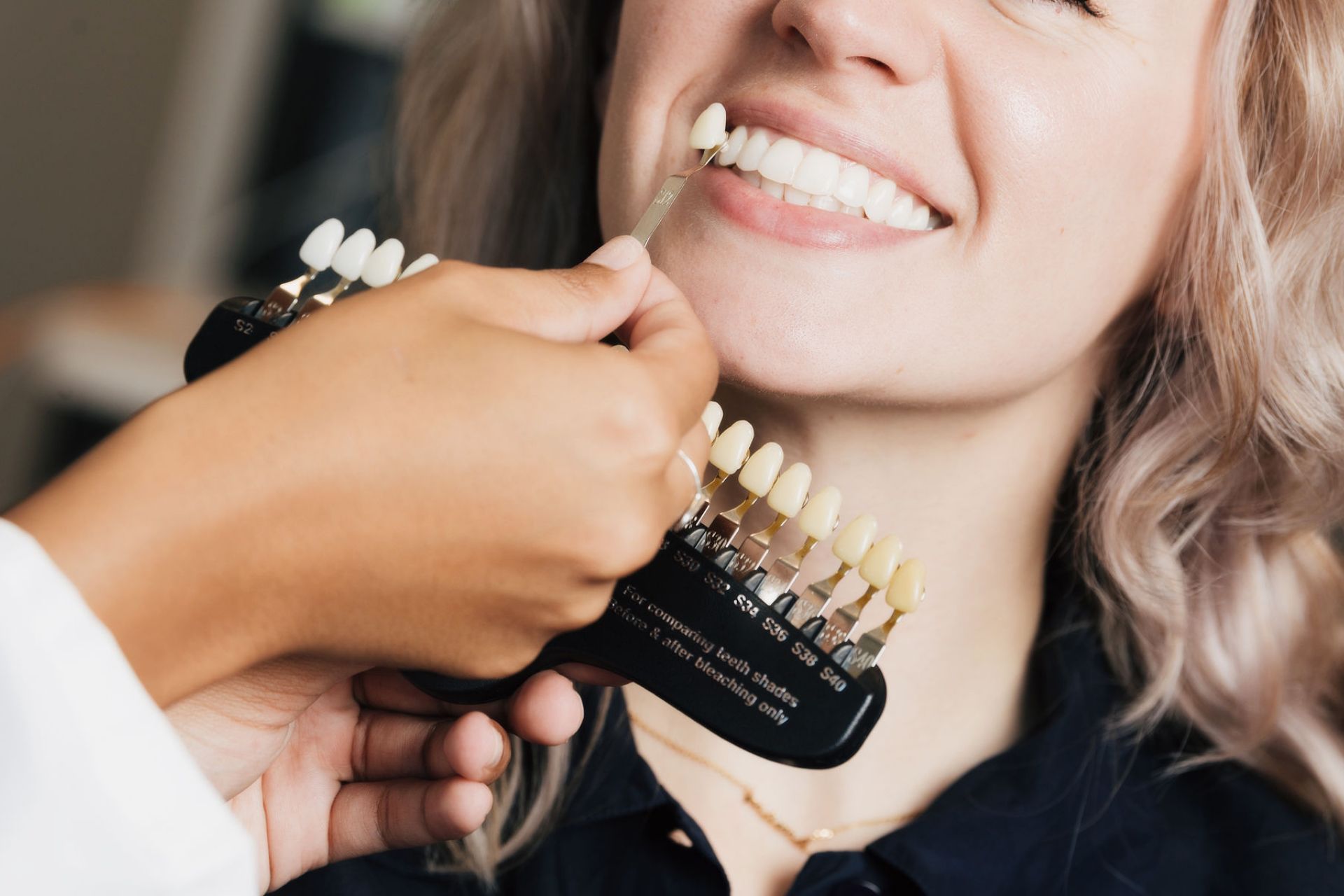 Dentist comparing shades of dental veneers to a smiling woman's teeth for color match.