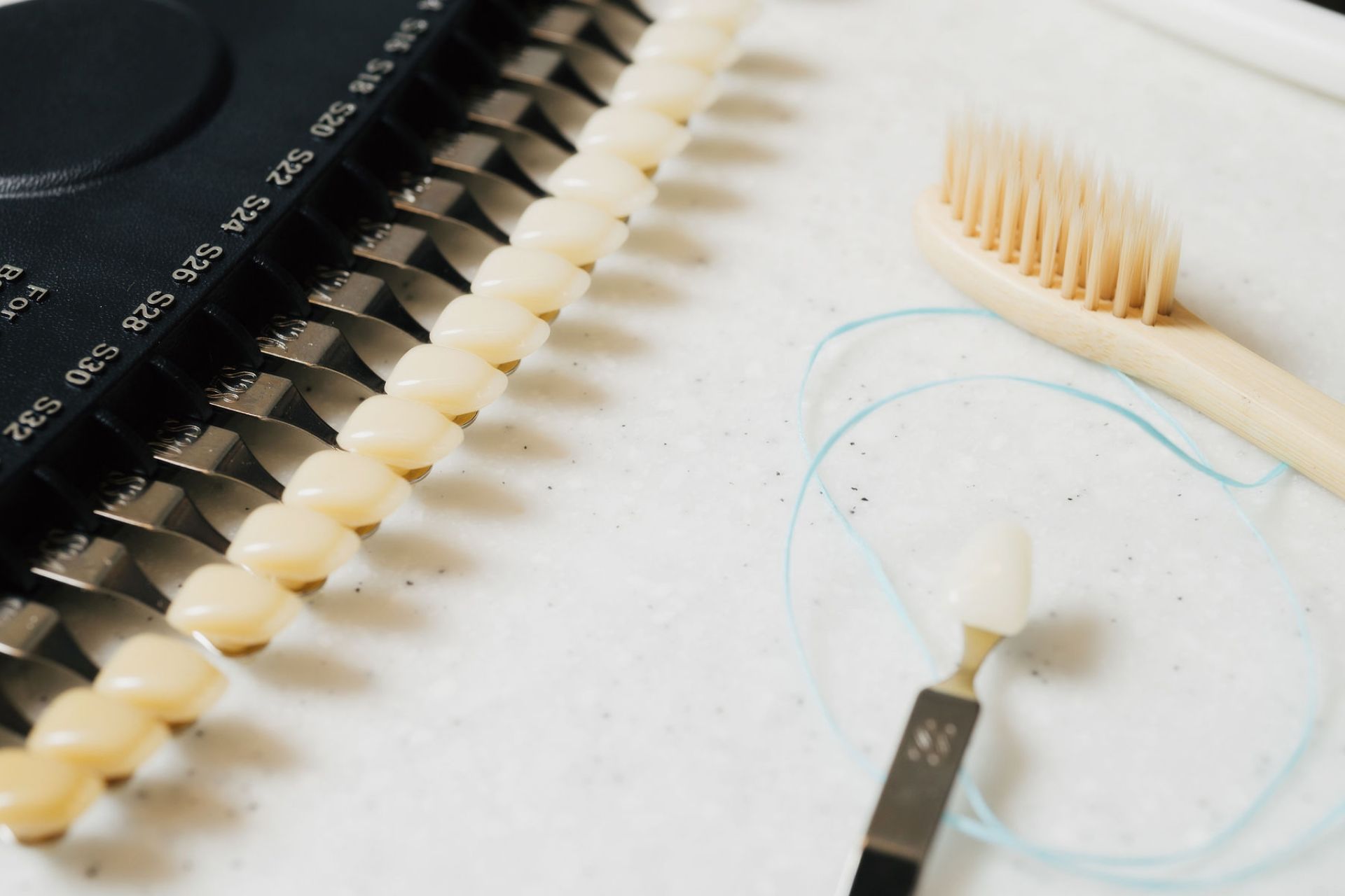 Dental shade guide with color tabs, a wooden toothbrush, and blue dental floss on a white surface.