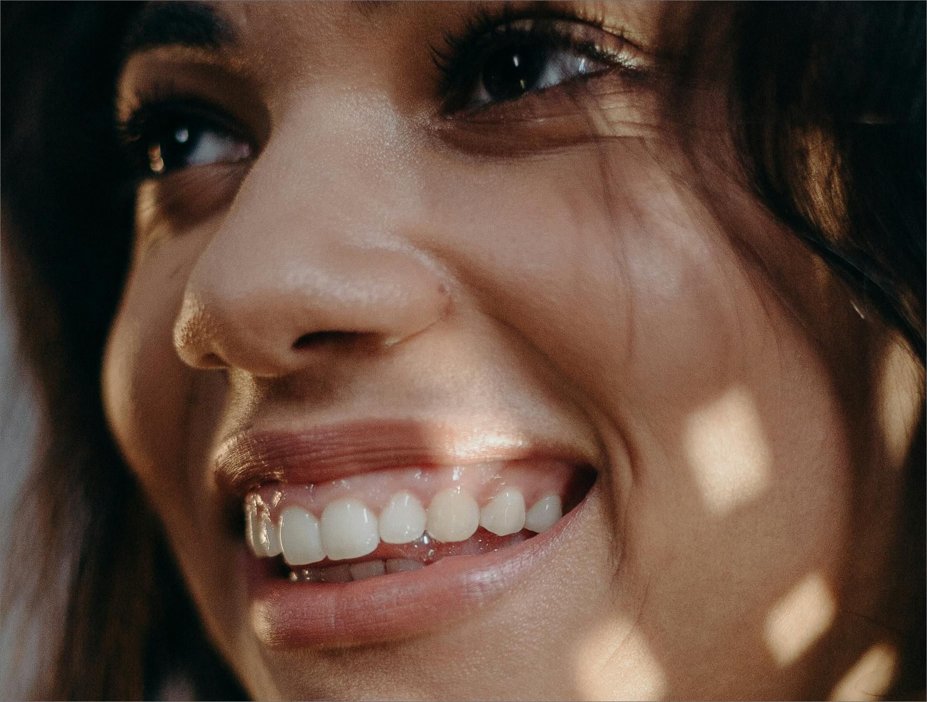 Close-up of a smiling woman showing her white teeth and dimples in warm light.