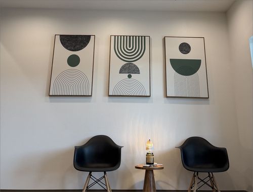 Two black modern chairs with wooden legs flanking a small round wooden table with a lit lamp.