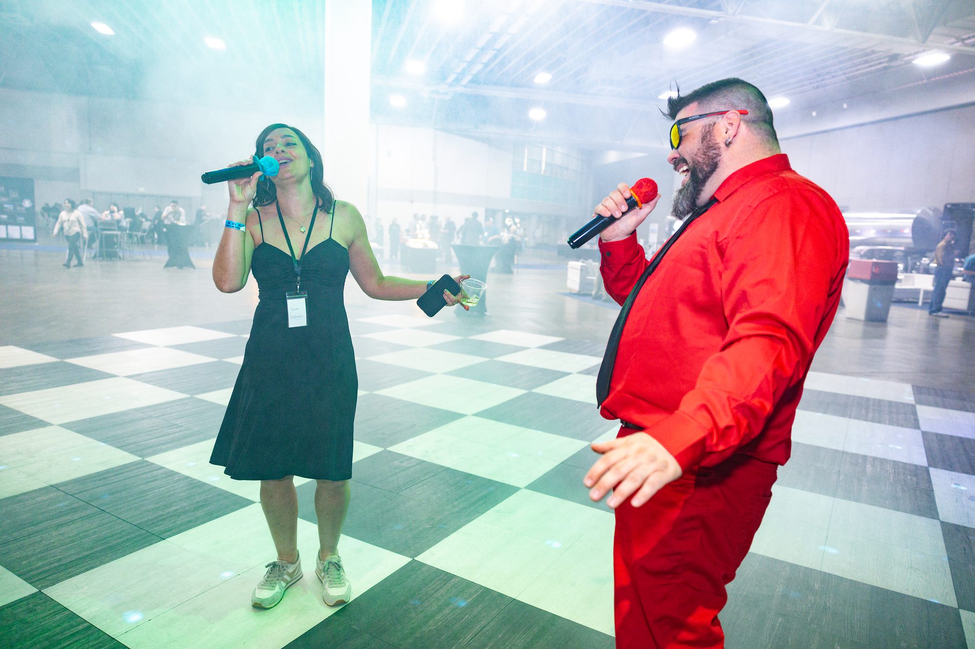 Two hosts with microphones presenting on an event floor