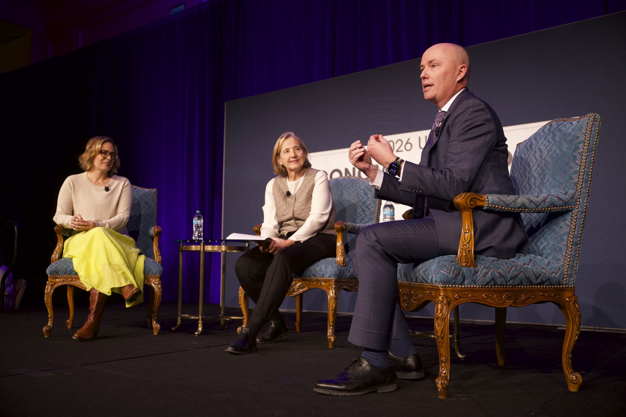 Three panelists seated on stage under purple lighting during a panel discussion