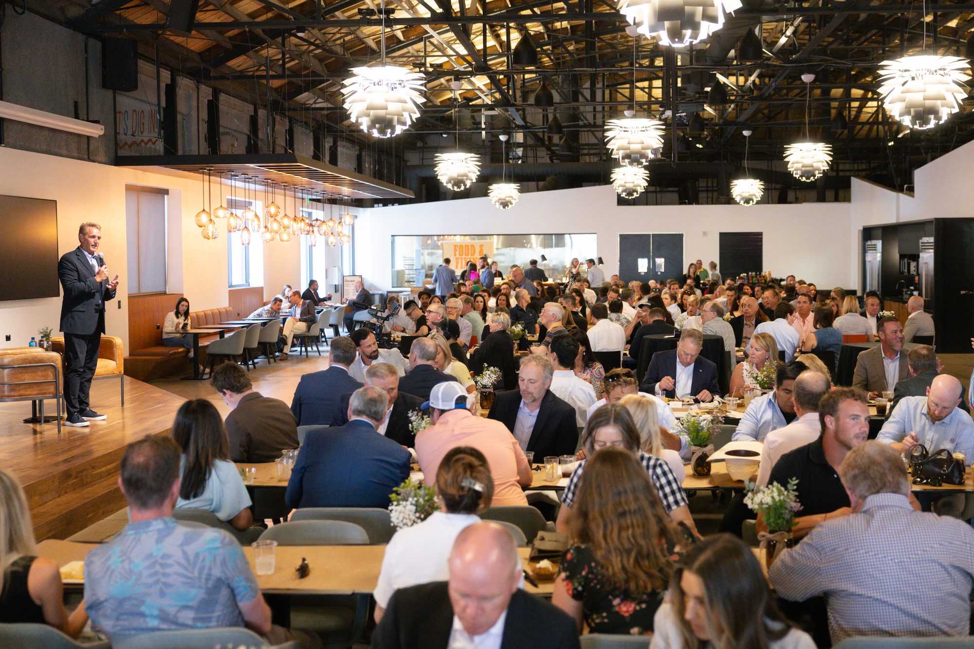 Speaker addressing guests seated at dinner tables during an evening program