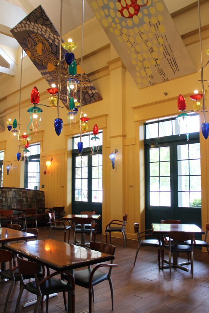 Tall ceilings, brown tables and chairs under colorful glass lighting fixtures at Saratoga Springs restaurant The Artist's Palette
