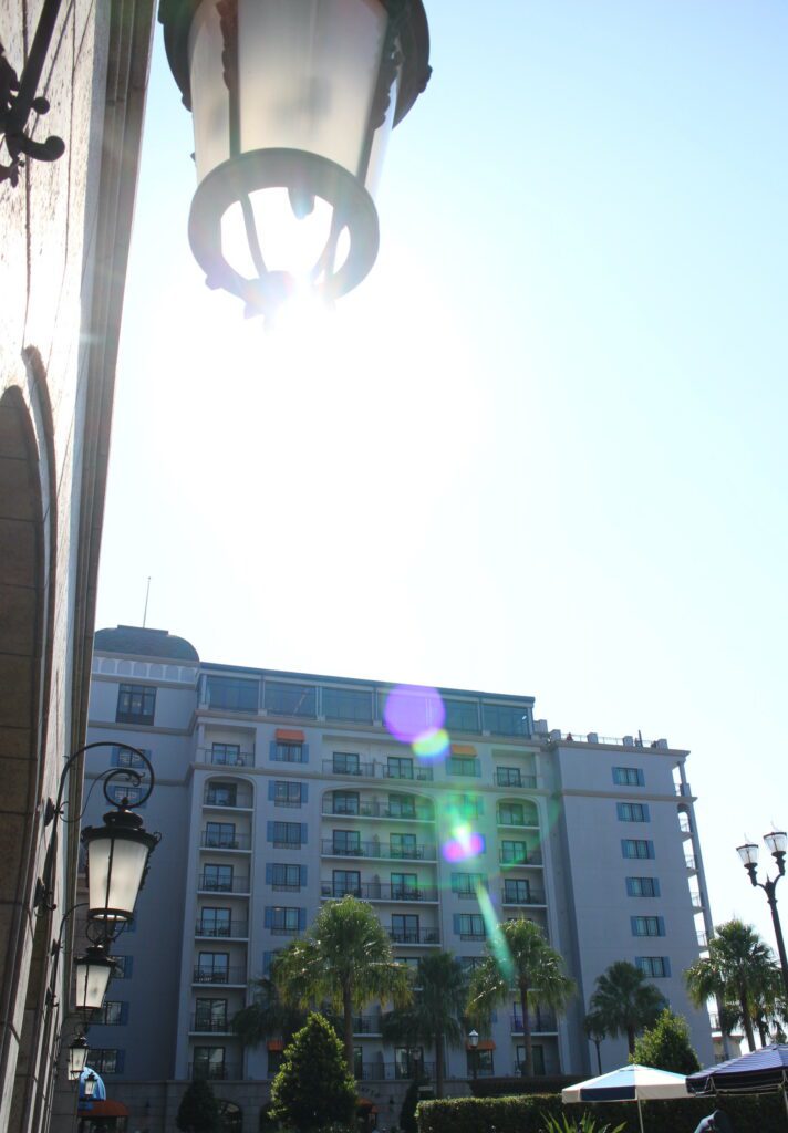 Disney's Riviera Resort tall building with gray stones and the sun shining over it with a solar flare. On the top of the building is Riviera resort restaurant and lounge Topolino's Terrace.