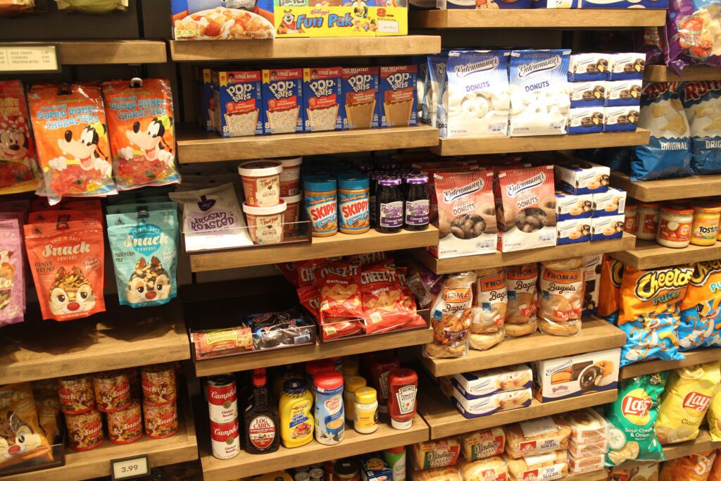 A wall of grocery items like peanut butter, donuts, crackers, soup and nut mixes at Disney's Riviera Resort lobby gift shop.