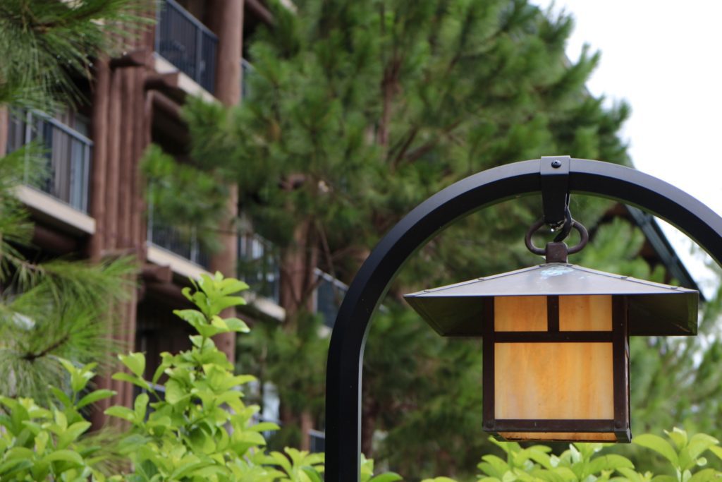 A black, craftsman style lantern hangs in front of trees and Copper Creek Villas at Wilderness Lodge.