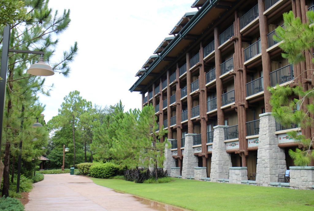 A sidewalk and lots of green landscaping in front of the wood and stone designed Copper Creek Villas building at Wilderness Lodge.