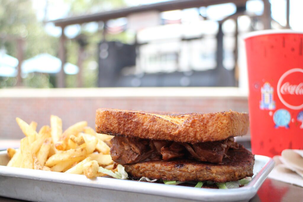 Regal Eagle Burger Meal with fries on a silver tray outdoors next to a Disney Coca Cola red cup. An example of what you might eat with Disney World vacation packages that include the Disney Dining Plan.