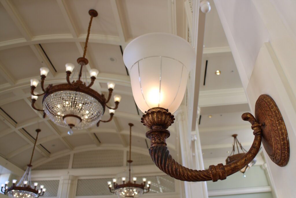 A golden, bronze, wall sconce with a frosted glass shade in the lobby of Disney's BoardWalk Resort where selling Disney Vacation Club Membership is possible