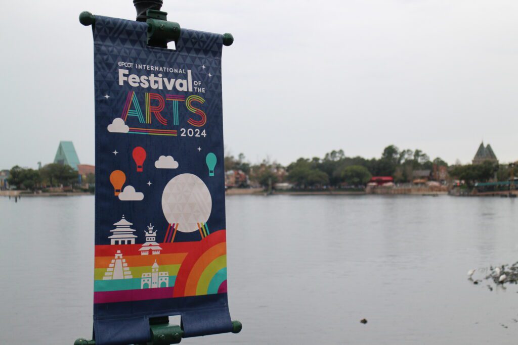 a colorful EPCOT Festival of the Arts sign in front of World Showcase Lagoon on a dreary day