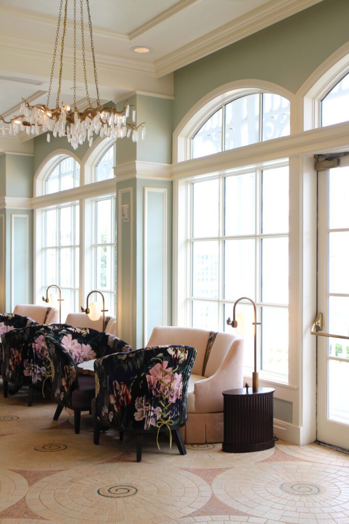 A bright interior with tall windows and light pink and patterned floral furnture pieces