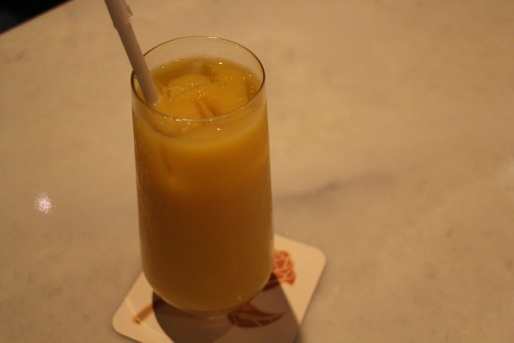 Enchanted Rose glass of orange juice on a marble style table with a rose coaster under it.