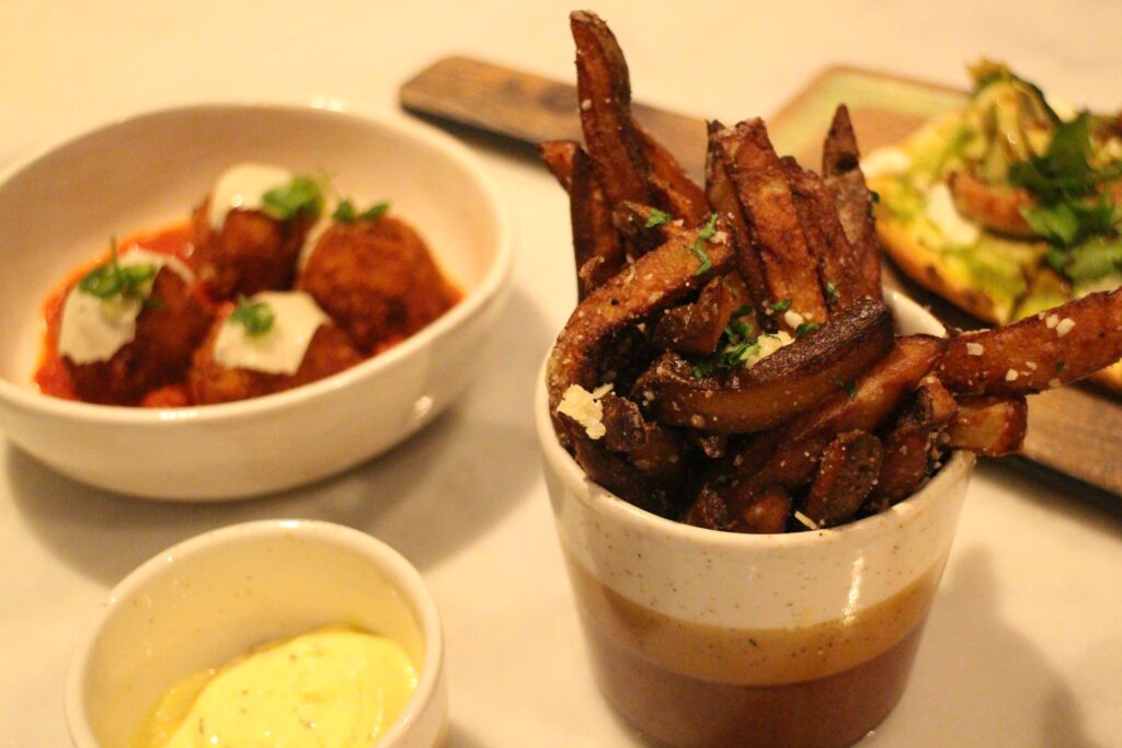Truffle fries from Enchanted Rose pictured with sauce and surrounded by other appetizers out of focus.