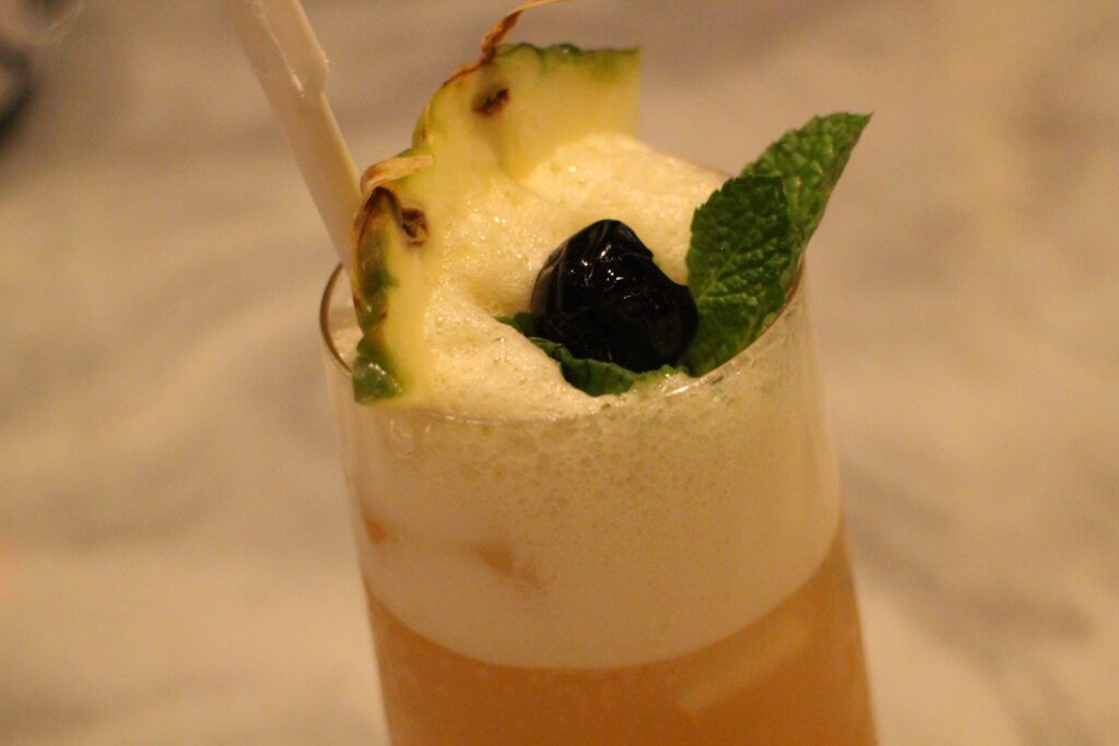 Enchanted Rose Island Rose drink in a glass with a pineapple on top.