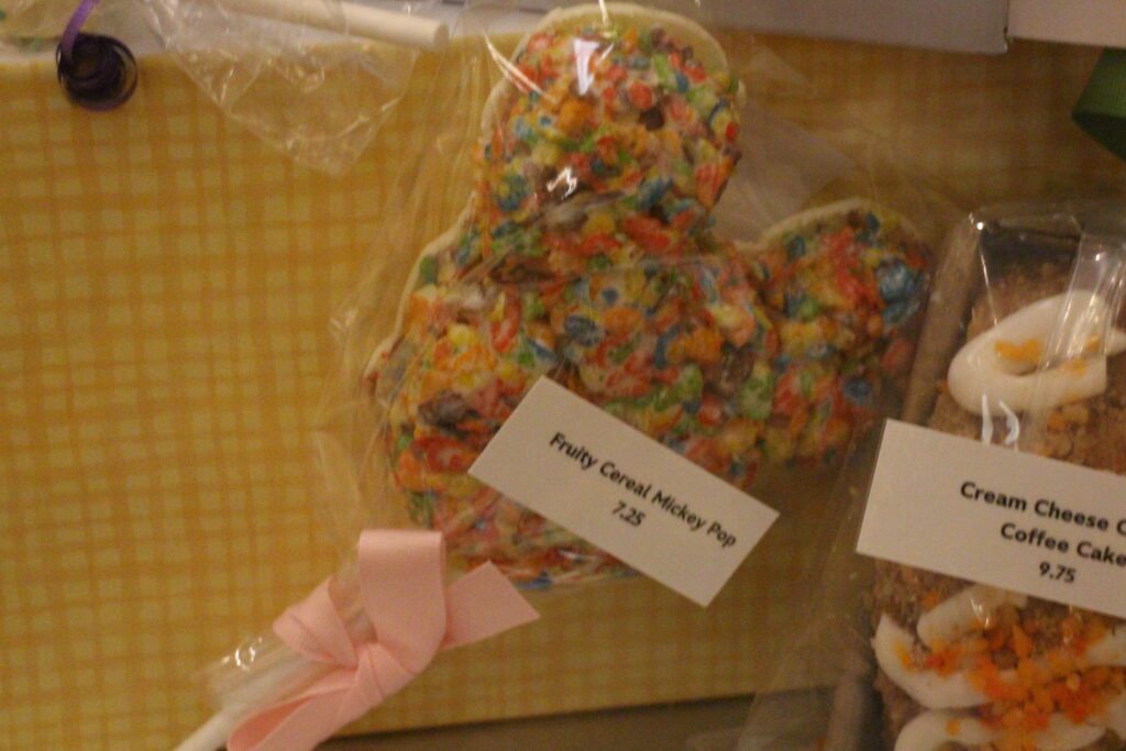 A colorful, Mickey crispy treat on a stick in a clear wrapping with a pink bow.