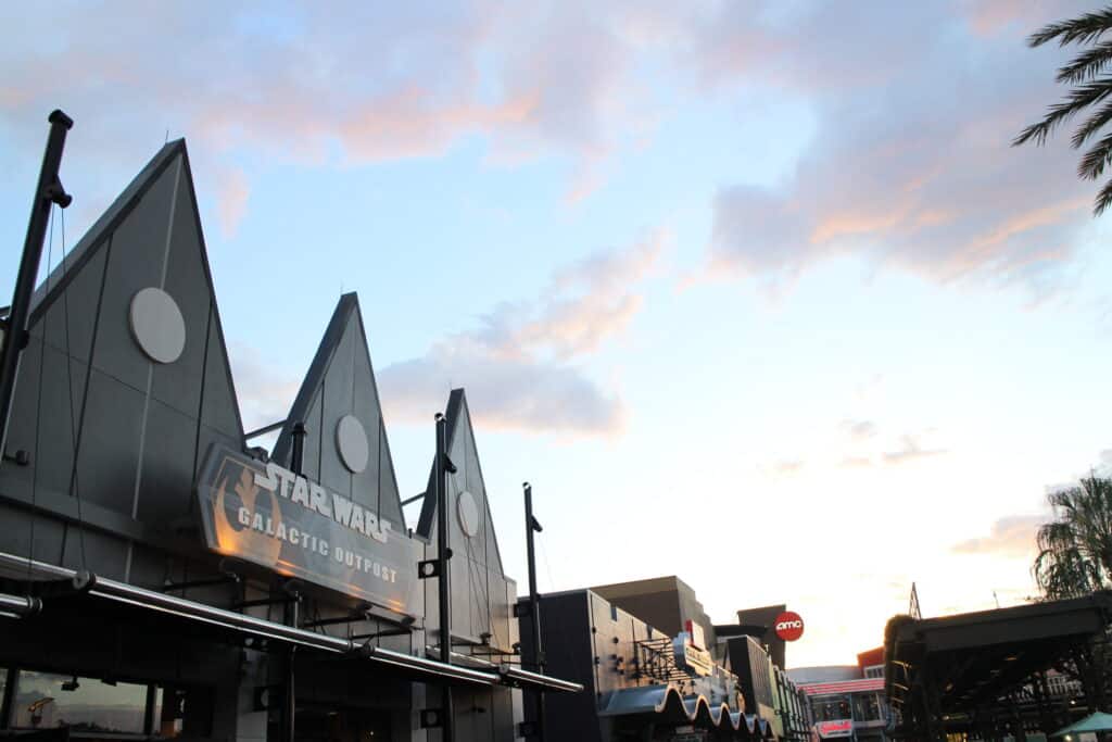 Disney Springs West Side store rooftops in front of a pastel sunset sky.