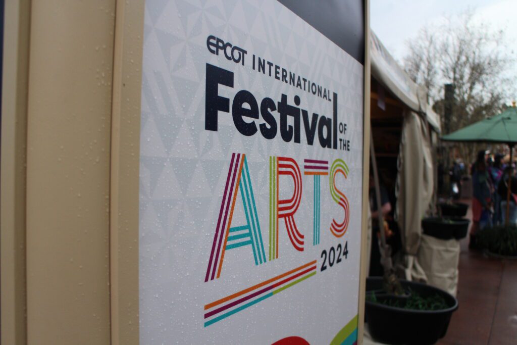 A sign that says Epcot Festival of the Arts 2024 with rain droplets on it.