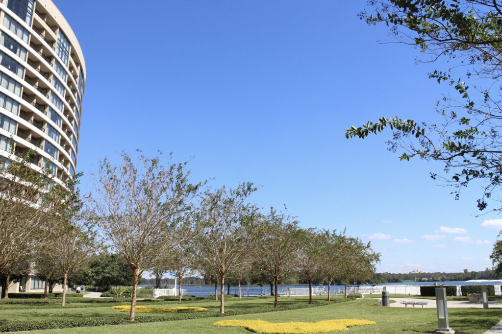 Green grass meets a blue sky next to the multi-story Bay Lake Tower building that overlooks a lake.