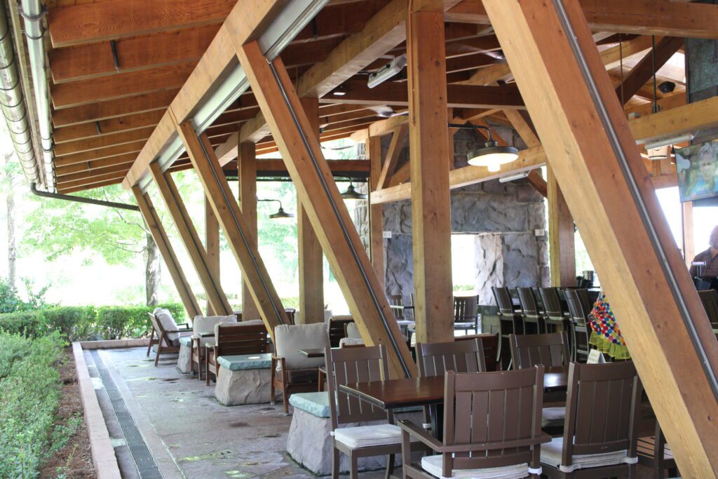 Geyser Point Bar and Grill at Disney's Wilderness Lodge with outdoor seating under a large covered roof, surrounded by greenery.