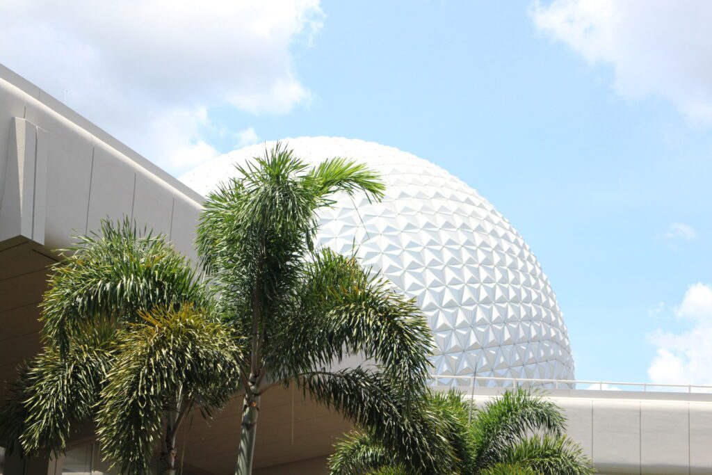 A sunny Florida day with a blue sky, palm trees and the top of the Spaceship Earth attraction peeking through.